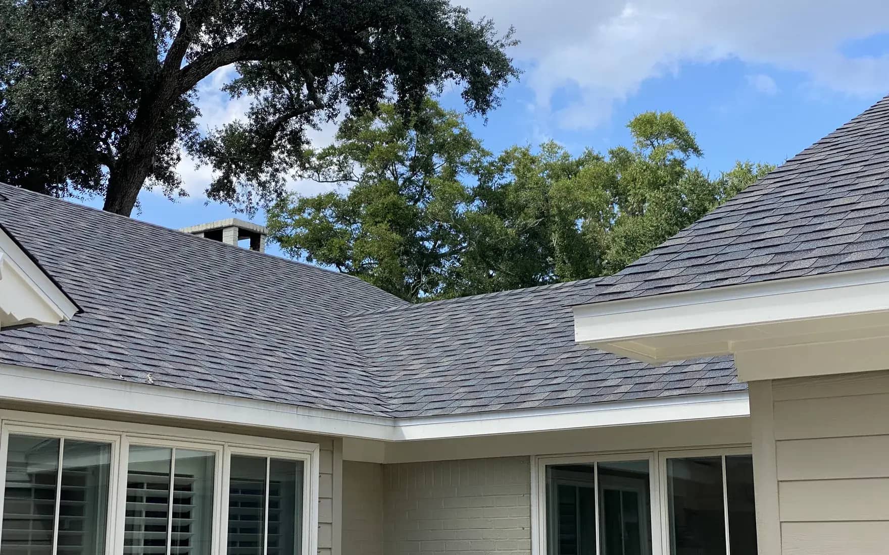 Finished gray architectural shingle roof with a hip and valley on a Baldwin County home, live oaks overhead.
